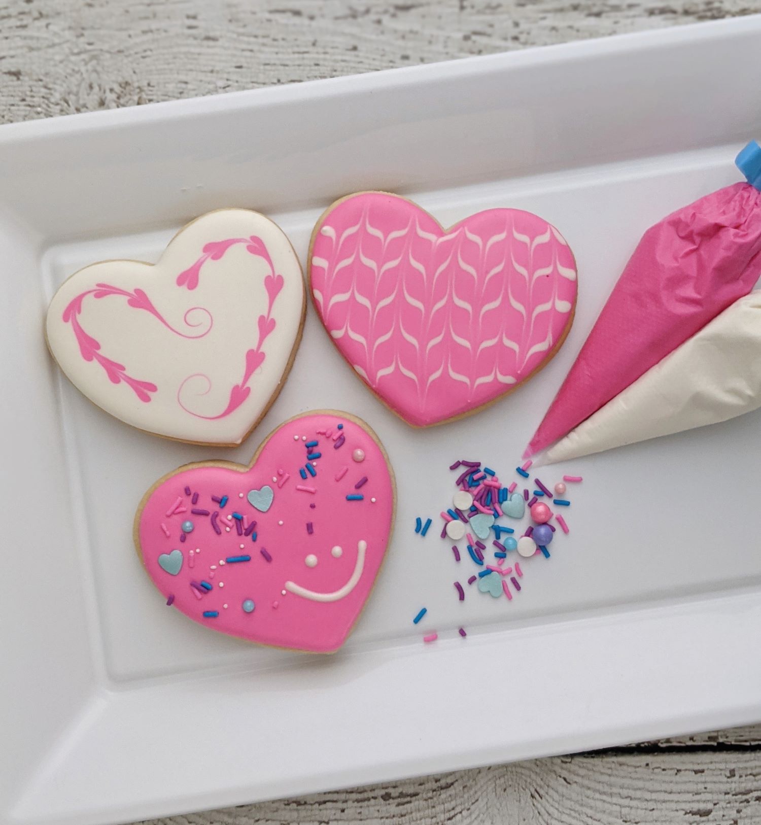 Pink heart biscuits pictured with piping bags and sprinkles